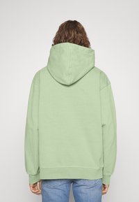 Sudadera con capucha de color verde menta hecha de algodón, con una capucha espaciosa, hombros caídos y un ajuste relajado, combinada con pantalones vaqueros de mezclilla azul claro.
