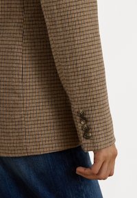 Gekruiste bruine blazer met een gestructureerde stof, vierknopen-manchetten en een getailleerde pasvorm, gecombineerd met denim.