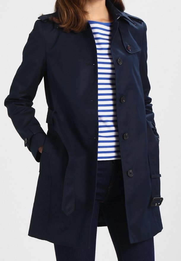 Marinblå trenchcoat med klassisk design, knäppning med knappar och V-formad krage. Tyget ser slätt ut och har ett skärp i midjan.