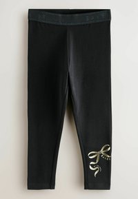 Leggings noirs en tissu extensible ; dotés d'un ruban doré brillant et d'un texte de marque sur le bas à gauche ; taille élastique en haut.