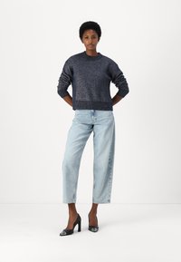 Pullover blu navy scintillante, vestibilità rilassata, colletto tondo, polsini a coste. Jeans azzurri chiari con gamba dritta e vestibilità rilassata. Scarpe nere con tacco alto e dettagli metallici.