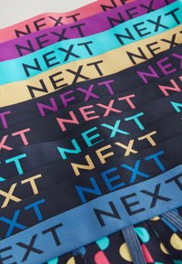 Des élastiques colorés disposés en rangées présentant le mot "NEXT" en gras, avec des couleurs alternées telles que rose, violet, bleu et jaune.