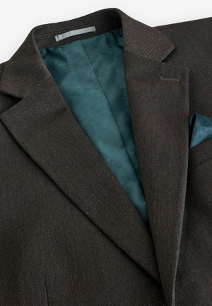 Blazer marrón texturizado con un forro interior en color teal que presenta un patrón geométrico. Detalles notables incluyen solapas y un pañuelo de bolsillo.