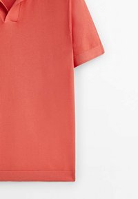 Polo à manches courtes corail avec un col en maille et un ourlet côtelé, présenté sur un fond blanc.