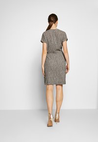 Robe à manches courtes avec un motif texturé noir et blanc, silhouette ajustée, longueur genou, accompagnée de talons métalliques à brides.