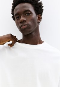 Hvid bomulds T-shirt, korte ærmer, rund halsudskæring, blød tekstur, let slid ved kraven, slidt afslappet.