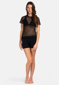 Czarna siateczkowa bluzka z krótkimi rękawami na czarnym, dopasowanym biustonoszu, w zestawieniu z czarnymi szortami. Prosty krój z przezroczystymi i jednolitymi panelami materiału.