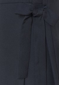 Detail zblízka na texturovanou tmavou látku s úhledně uvázanou mašlí na pravé straně.