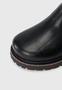 Černá kožená kotníková bota s kulatou špičkou a texturovaným povrchem. Disponuje odolnou gumovou podešví s mírným platformovým efektem a viditelným šitím.