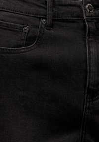 Gros plan d'un jean en denim noir montrant la poche avant, la boucle de ceinture, le bouton et les coutures détaillées sur le tissu.