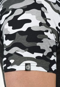 Short-sleeve t-shirt featuring a gray, black, and white camouflage pattern with a black label stitched at the hem. Cotton material.