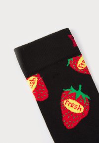 Svarta strumpor med röda jordgubbar, gula detaljer och gröna blad, med en strukturerad stickning, där ordet "fräsch" finns på jordgubbarna.
