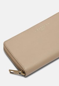 Cartera de cuero beige con un acabado texturizado, cremallera y logotipo en tono dorado. Presenta un diseño delgado y un cierre con cremallera práctico.