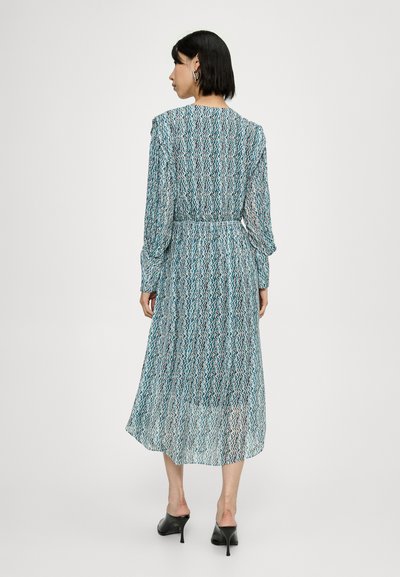 Rochie lungă ușoară cu un model valurit în nuanțe de albastru și alb. Dispune de o talie strânsă și mâneci lungi, accesorizată cu pantofi cu toc înalt de culoare neagră.