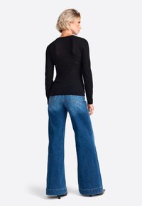 Schwarz langärmliges geripptes Oberteil kombiniert mit weitgeschnittenen blauen Denim-Hosen, die eine hohe Taille und sichtbare Nähdetails aufweisen.