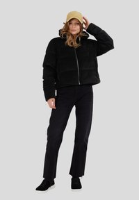 Musta corduroy-puffatakki, jossa on vetoketjusulku, huppu ja tikattu kuvio, yhdistettynä mustiin farkkuihin ja mustiin lenkkiareihin. Vaalea lippalakki.