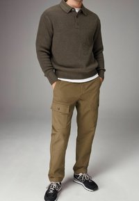 Olivengroen geribde trui met een kraag en drie knopen, gecombineerd met khaki cargobroek met zijzakken en zwarte sportieve schoenen.