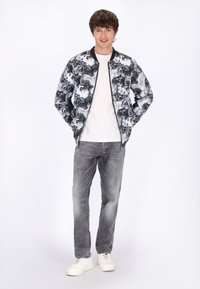 Zwart-wit marmerpatroon bomberjack, met rits aan de voorkant, gecombineerd met een wit T-shirt, grijze jeans en witte sneakers.