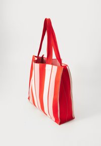 Red and pink striped tote bag with sturdy fabric, rectangular shape, soft texture, and two top handles. Features a minimalist design.
