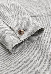 Gray and white striped shirt cuff featuring a button made of a light-colored material, with a smooth texture and tailored design.