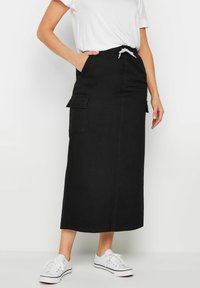 Gonna maxi in denim nero con due tasche laterali, vita elasticizzata con cordoncino e taglio dritto. Abbinata a sneakers bianche.