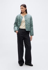 Πράσινο bomber μπουφάν με ραμμένη υφή, στρογγυλή λαιμόκοψη και κουμπιά με πατρόν, συνδυασμένο με μπεζ τοπ και φαρδιά σκούρα τζιν παντελόνια.