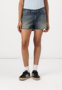 Denim short in een vervaagde blauwe kleur, met rafelige uiteinden, een vijf-pocket ontwerp en een aansluitende pasvorm. Gecombineerd met zwarte sneakers.
