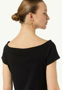 Czarny top na jedno ramię z krótkimi rękawami, gładka faktura i wyraźny dekolt. Złote kolczyki w kształcie kół podkreślają design.