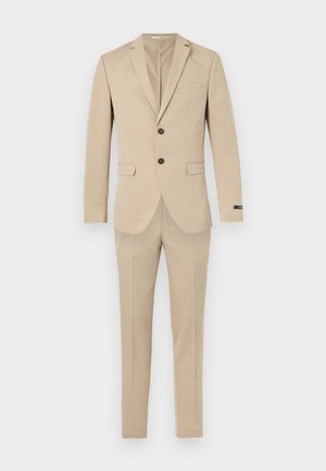 Bézs színű férfi öltöny, kétgombos blézerrel, bevágott hajtókával, zsebfedőkkel és hozzáillő, karcsúsított szabású nadrággal, fehér háttéren.