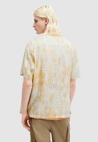 Camicia a maniche corte con un leggero motivo pitonato, caratterizzata da tonalità di giallo e beige. Realizzata in un tessuto morbido e leggero con una vestibilità comoda.
