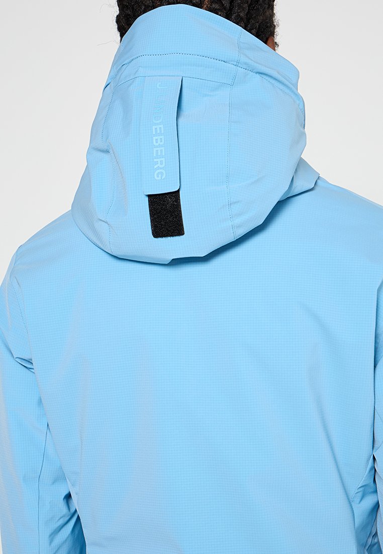 Niebieska wodoodporna kurtka z teksturowanym wykończeniem, z dopasowanym kapturem, regulowanym paskiem i detalem logo na plecach.