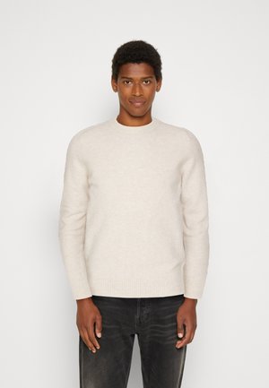 Lichtbeige trui met ronde hals, geribbelde manchetten en zoom. Zachte textuur, getailleerde stijl, gecombineerd met donkere jeans.