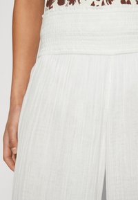 Bílé, plisované látkové kalhoty se smockovaným elastickým pasem; lehká textura; jemně zpracované pro měkký, splývavý vzhled.