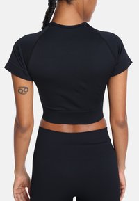 Czarny dopasowany sportowy top na krótki rękaw o gładkiej teksturze i skróconym kroju, zestawiony z czarnymi legginsami o wysokim stanie.