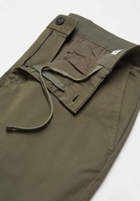 Pantalon vert olive avec fermeture à boutons, braguette zippée et taille à cordelette visible sur fond blanc.