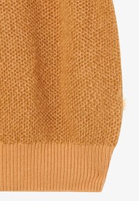 Pull en tricot avec un motif en nid d'abeille texturé en jaune moutarde. Équipé d'un ourlet côtelé et d'une petite étiquette de marque sur le côté.
