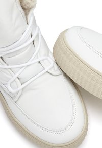 Weiße Leder-Sneaker mit einer strukturierten, beigen Gummisohle und weißen Schnürsenkeln. Das Innere verfügt über eine weiche Polsterung für zusätzlichen Komfort.