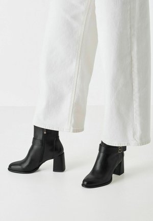 Black leather ankle boots with a pointed toe and block heel, featuring a side zipper and a strap with a circular metal accent.