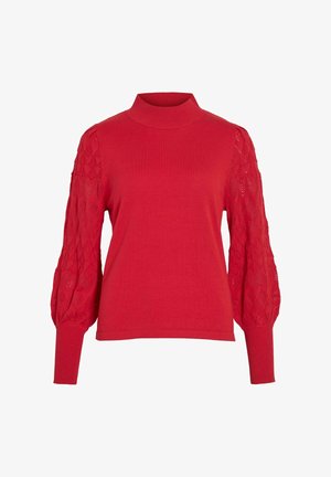 Punane kõrge kaelusega kootud spordipluus, millel on ühtlane kudumine ja mustrilised, tekstureeritud puffsleevid. Ribitud mansetid ja äär.