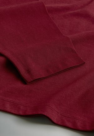 Burgundi pikkade varrukatega särk, millel on pehme ja sile tekstuur ning lihtne disain. Nähtav õmblusdetail varruka ja serva juures.