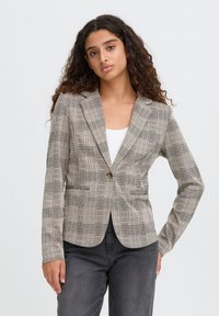 Béžový károvaný blazer s přiléhavým střihem, s jedním knoflíkem, dvěma předními kapsami a texturovanou tkaninou.