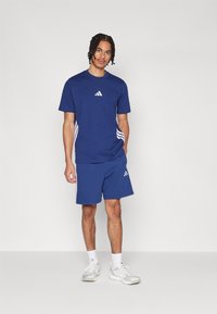 Blauw sport T-shirt en shorts gemaakt van ademend materiaal, met witte strepen aan de zijkanten en logo-accenten op de borst en shorts.