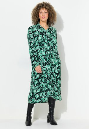 Schwarzes Kleid mit grünem Blumenmuster, langen Ärmeln, durchgehender Knopfleiste und fließender Silhouette, kombiniert mit kniehohen schwarzen Stiefeln.