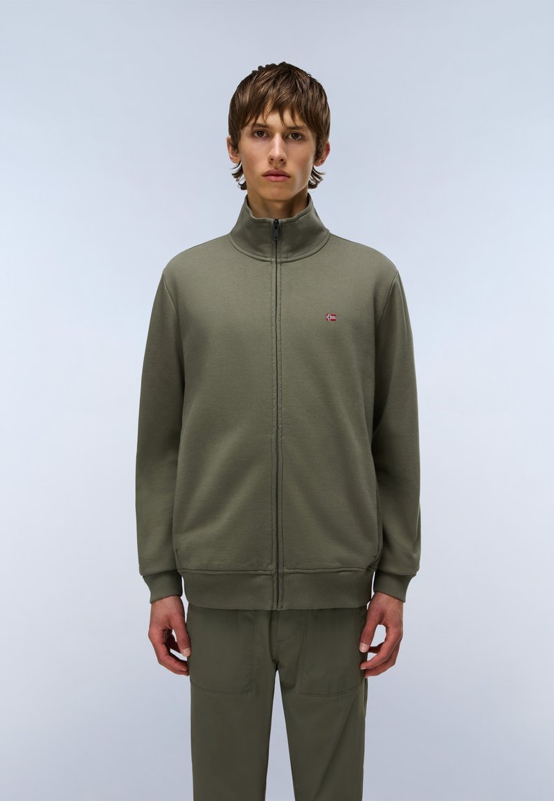 Sudadera con cremallera de color verde oliva y cuello alto, con puños y cinturilla acanalados, que presenta un pequeño logo en el lado izquierdo del pecho. Textura de tela suave.