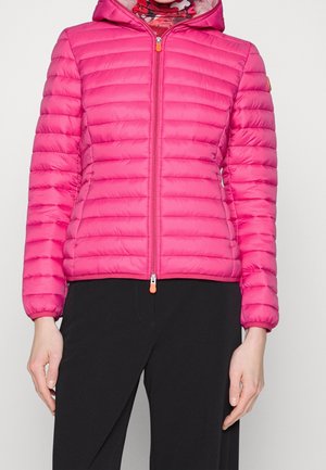 Pink padded jacket with a hood, featuring horizontal quilted design, mid-length zip closure, and orange zipper pull, paired with black pants.