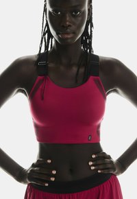 Sportsbh i levende rødt med sorte stropper og sidepaneler med teksturerede detaljer. Blødt, strækbart stof designet til komfort og støtte.