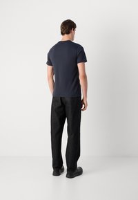 Cămașă cu mânecă scurtă de culoare bleumarin, croială lejeră, asortată cu pantaloni din denim negri cu croiala largă. Textură netedă, design simplu și fără logo-uri vizibile.