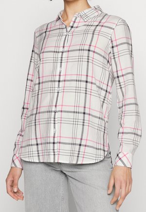 Chemise blanche à boutons avec motif à carreaux rose et gris portée avec un jean en denim gris clair sur une personne debout.