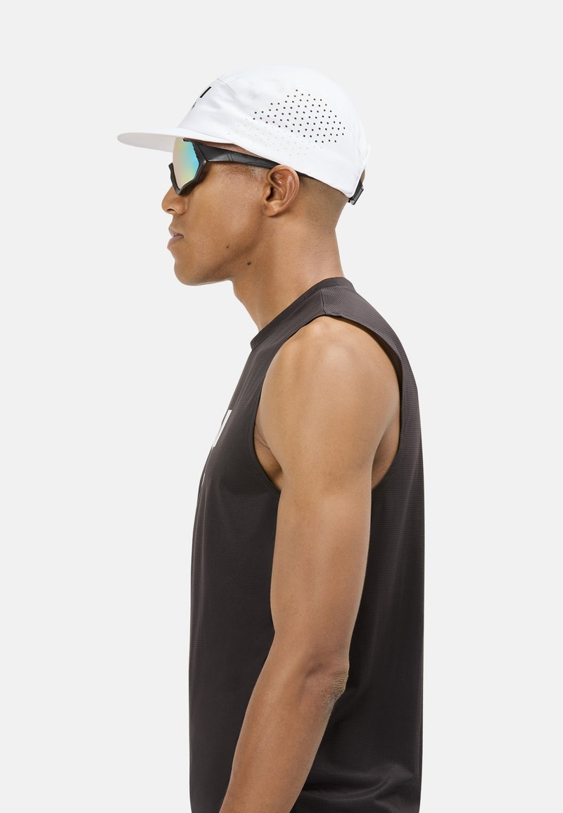 Gorra blanca con orificios de ventilación, gafas de sol espejadas, camiseta sin mangas negra. Vista de perfil que resalta texturas suaves y un ajuste atlético.