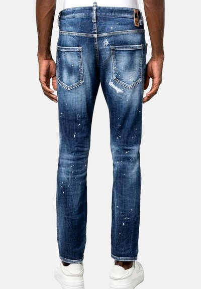 Denimjeans mit einem ausgebleichten, distressed blauen Finish, das Splatterdetails aufweist, fünf Taschen und einem geraden Bein Schnitt. Weiße Turnschuhe sind sichtbar.